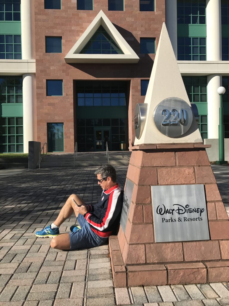 Disney author Jeff Noel sitting on ground writing on iPhone 